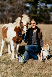 Woman kneeling with a mini pony and dog on each side, with a bag of Enjoy Yums mint treats on the ground – all-natural, heart-shaped treats for horses and dogs.